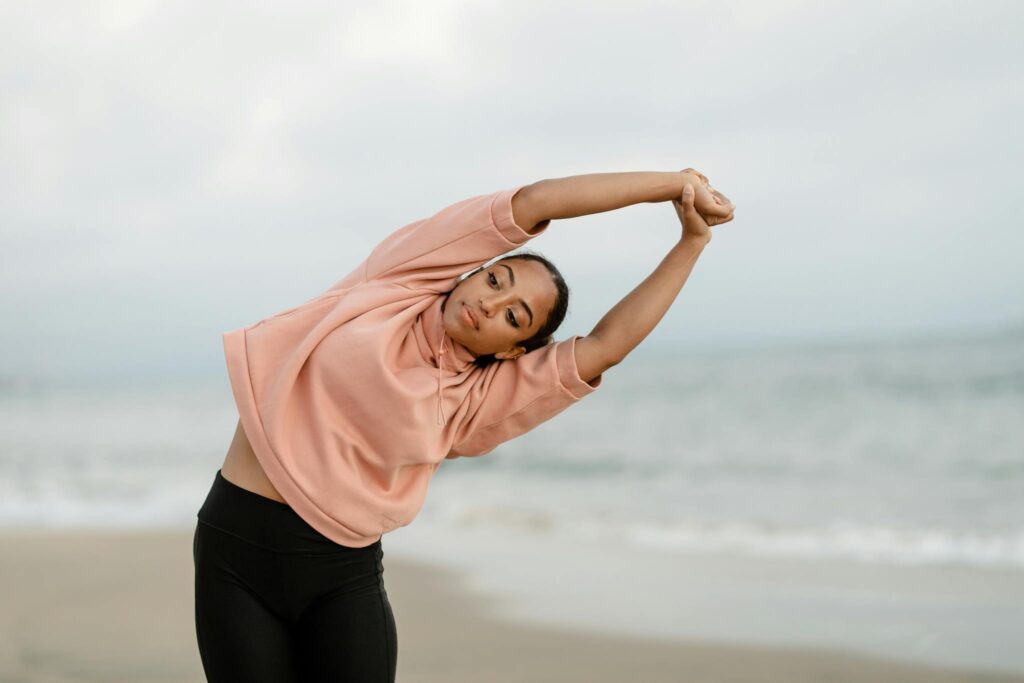 A woman performs a side stretch yoga pose on an ocean beach, promoting balance and confidence